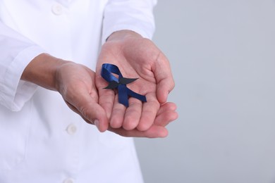 Prostate cancer awareness. Doctor holding blue ribbon with fake mustache on light grey background, closeup. Space for text