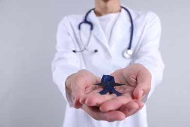 Prostate cancer awareness. Doctor holding blue ribbon with fake mustache on light grey background, closeup