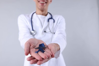 Photo of Prostate cancer awareness. Doctor holding blue ribbon with fake mustache on light grey background, selective focus