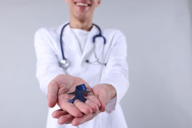 Prostate cancer awareness. Doctor holding blue ribbon with fake mustache on light grey background, selective focus