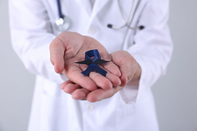 Photo of Prostate cancer awareness. Doctor holding blue ribbon with fake mustache on light grey background, closeup