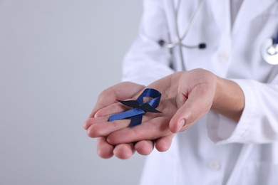 Photo of Prostate cancer awareness. Doctor holding blue ribbon with fake mustache on light grey background, closeup