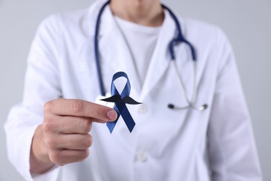 Photo of Prostate cancer awareness. Doctor holding blue ribbon with fake mustache on light grey background, closeup