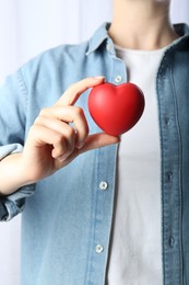 Woman holding red heart on light background, closeup