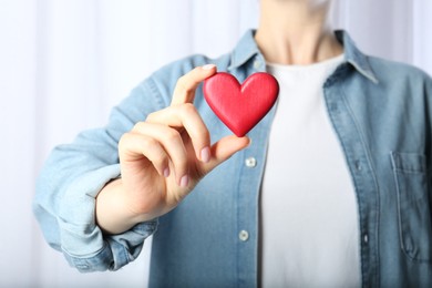 Woman holding red heart on light background, closeup