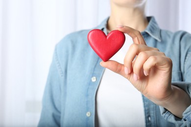 Woman holding red heart on light background, closeup