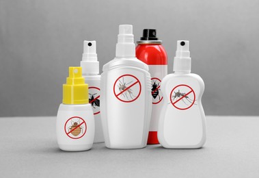 Different insect repellents in spray bottles on grey background