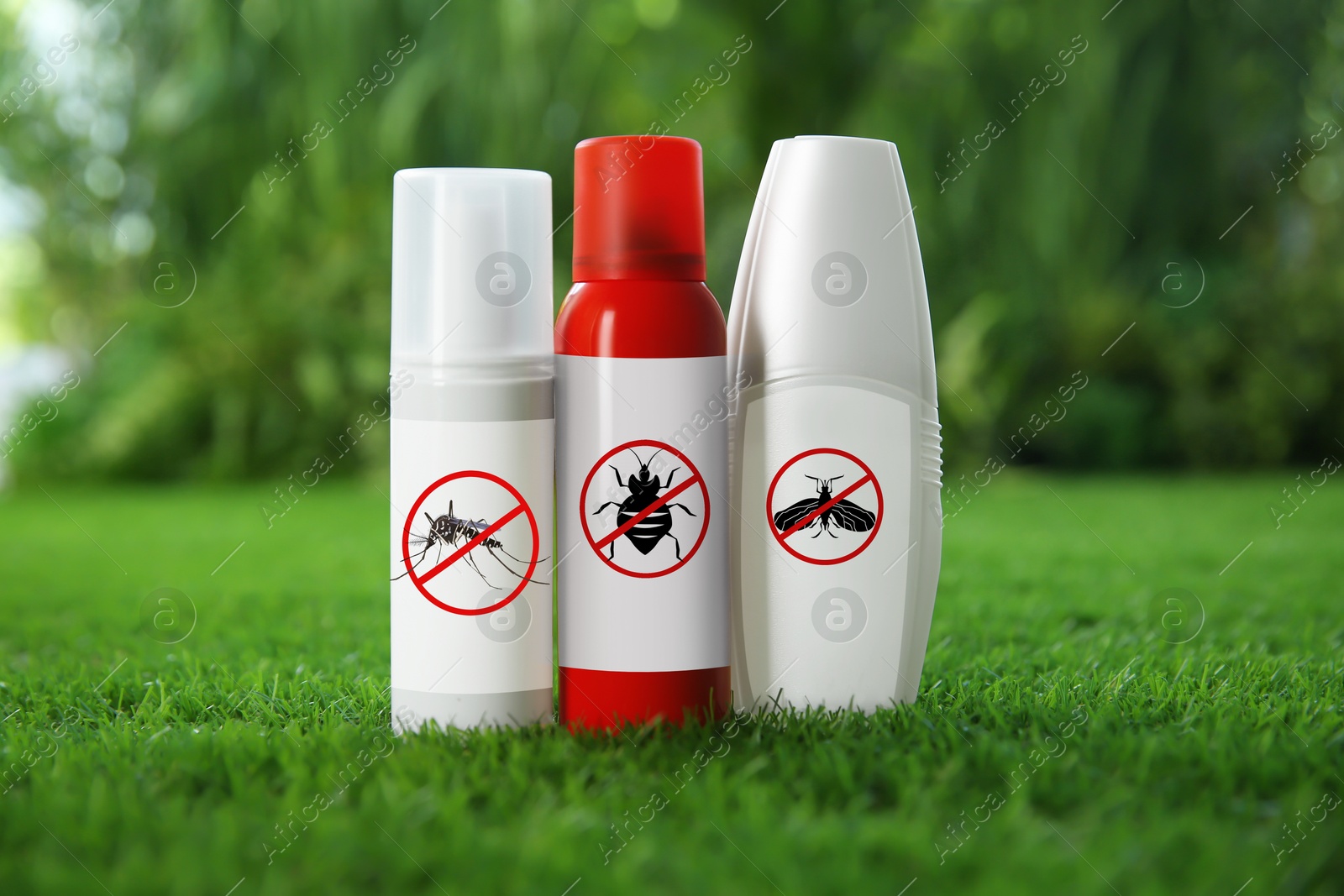 Image of Different insect repellents in spray bottles on green grass outdoors