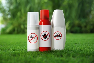 Different insect repellents in spray bottles on green grass outdoors