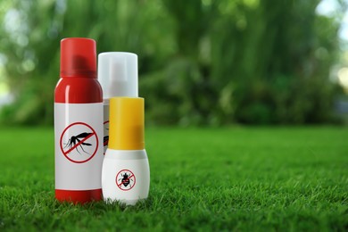 Different insect repellents in spray bottles on green grass outdoors, space for text