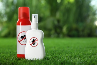 Different insect repellents in spray bottles on green grass outdoors, space for text