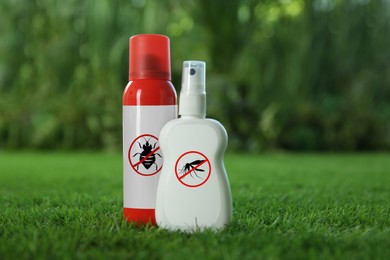 Different insect repellents in spray bottles on green grass outdoors, space for text