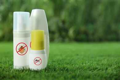 Image of Different insect repellents in spray bottles on green grass outdoors, space for text