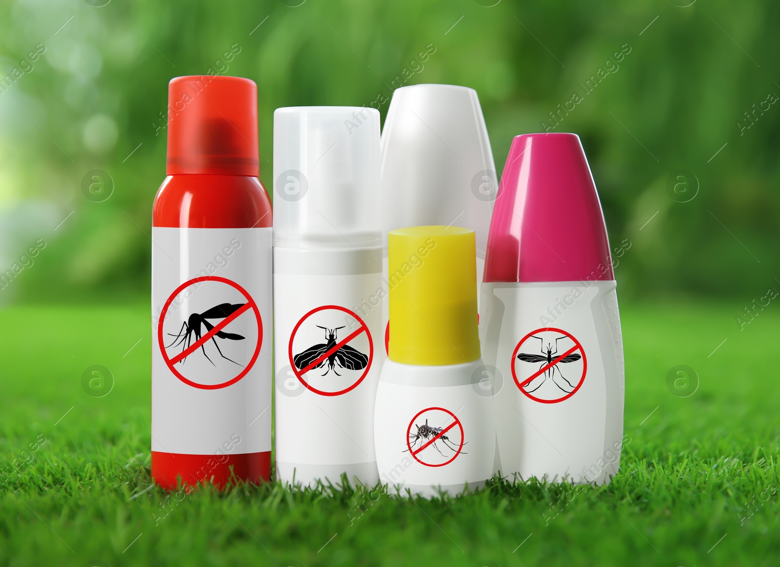 Image of Different insect repellents in spray bottles on green grass outdoors