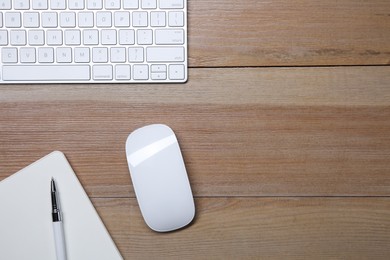 Wireless mouse, notebook, pen and computer keyboard on wooden table, flat lay. Space for text