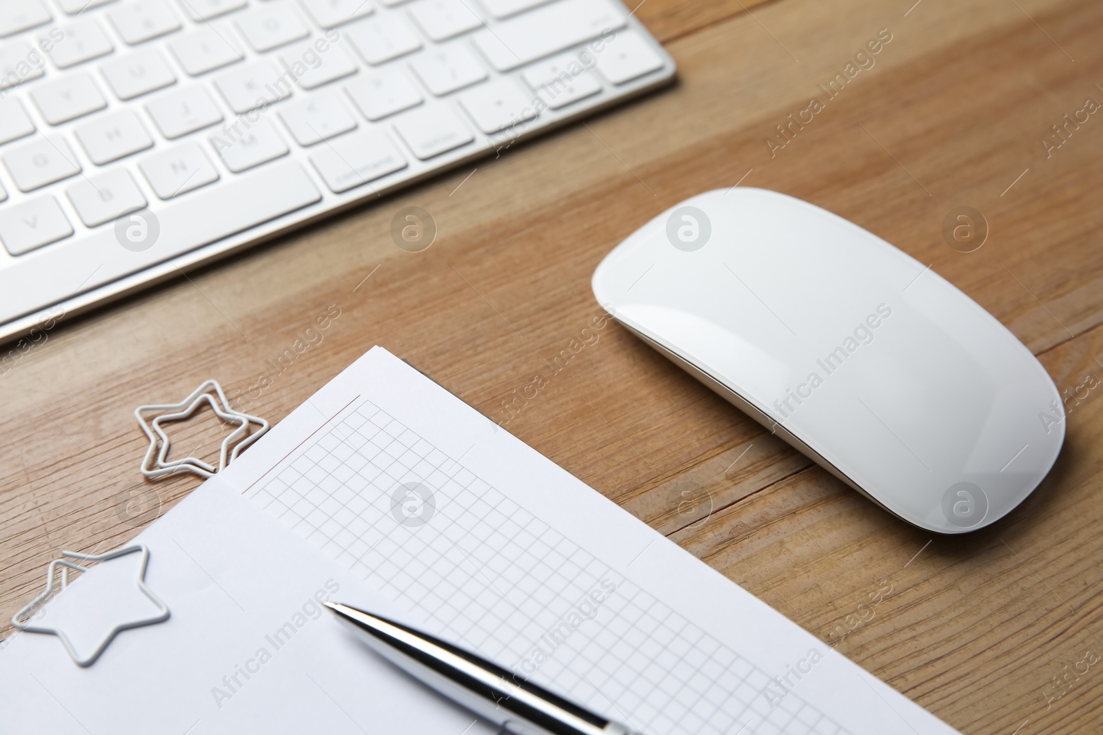 Photo of Wireless mouse, notebook, pen and computer keyboard on wooden table, closeup