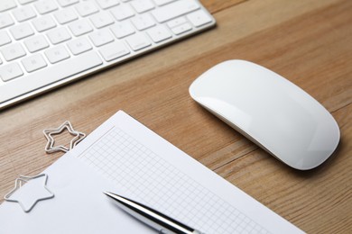 Wireless mouse, notebook, pen and computer keyboard on wooden table, closeup