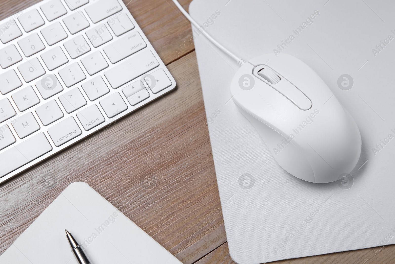 Photo of Wired mouse with mousepad, notebook, pen and computer keyboard on wooden table, above view