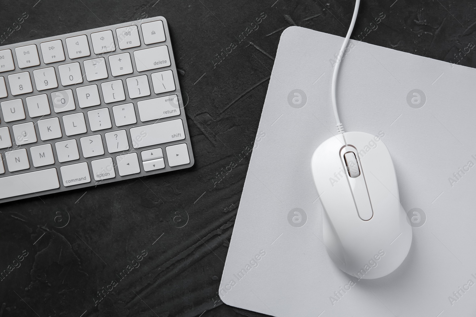 Photo of Wired mouse with mousepad and computer keyboard on dark textured table, flat lay