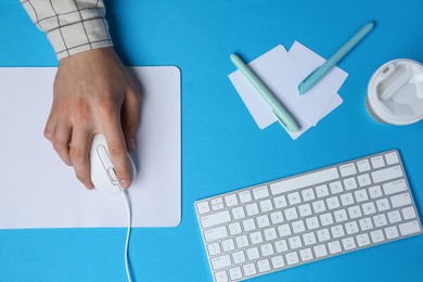 Photo of Man with mouse, takeaway cup, stationery and computer keyboard at light blue table, top view