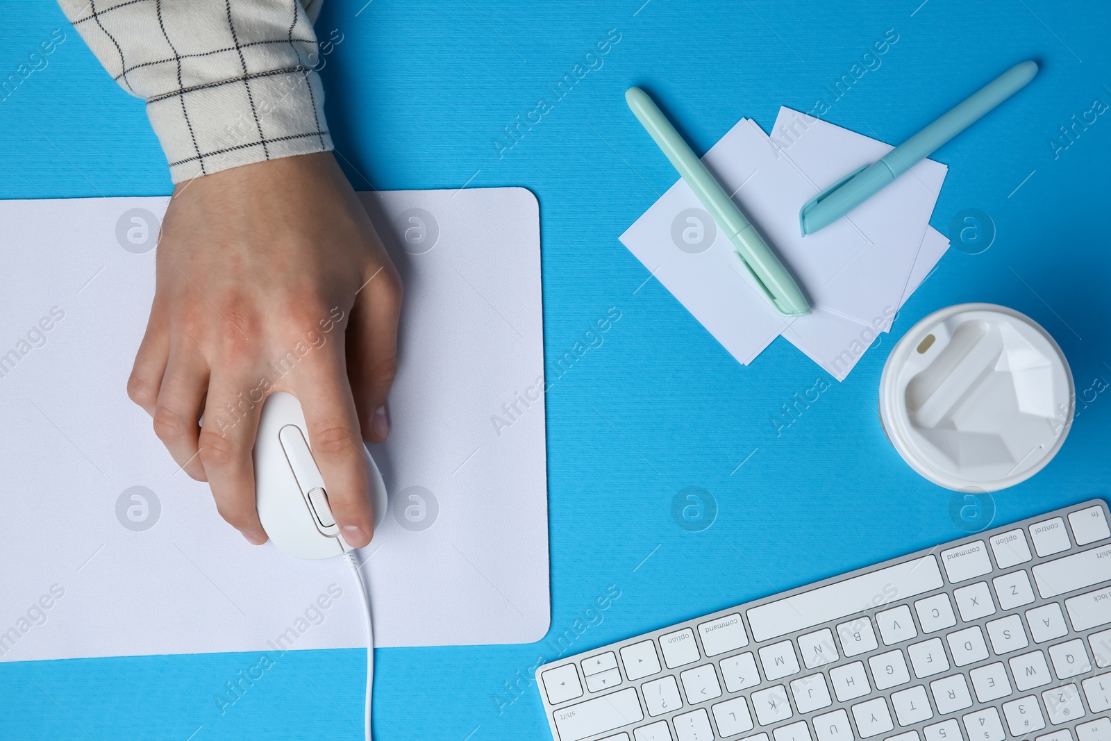 Photo of Man with mouse, takeaway cup, stationery and computer keyboard at light blue table, top view