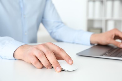 Photo of Man working with wireless mouse and laptop at white table indoors, closeup