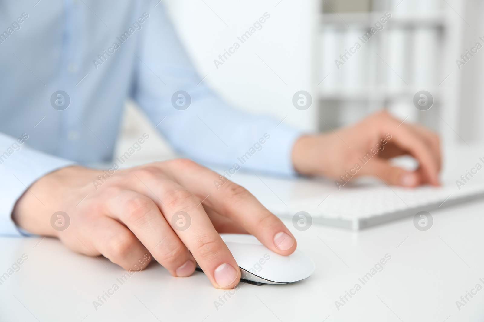 Photo of Man working with wireless mouse and computer keyboard at white table indoors, closeup