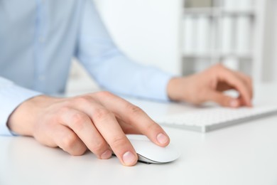 Photo of Man working with wireless mouse and computer keyboard at white table indoors, closeup