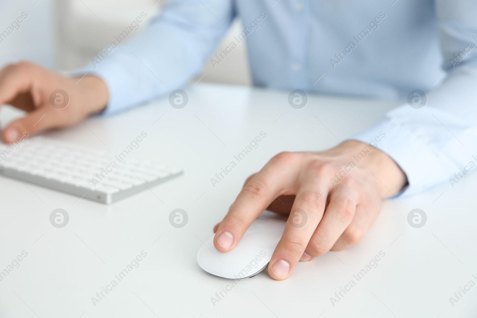 Photo of Man working with wireless mouse and computer keyboard at white table indoors, closeup