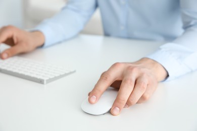 Man working with wireless mouse and computer keyboard at white table indoors, closeup