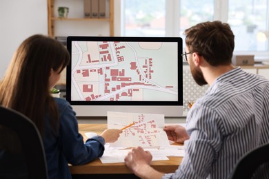 Cartographers working with cadastral maps at table in office, back view