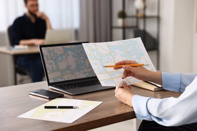 Cartographer working with cadastral maps at wooden table in office, closeup