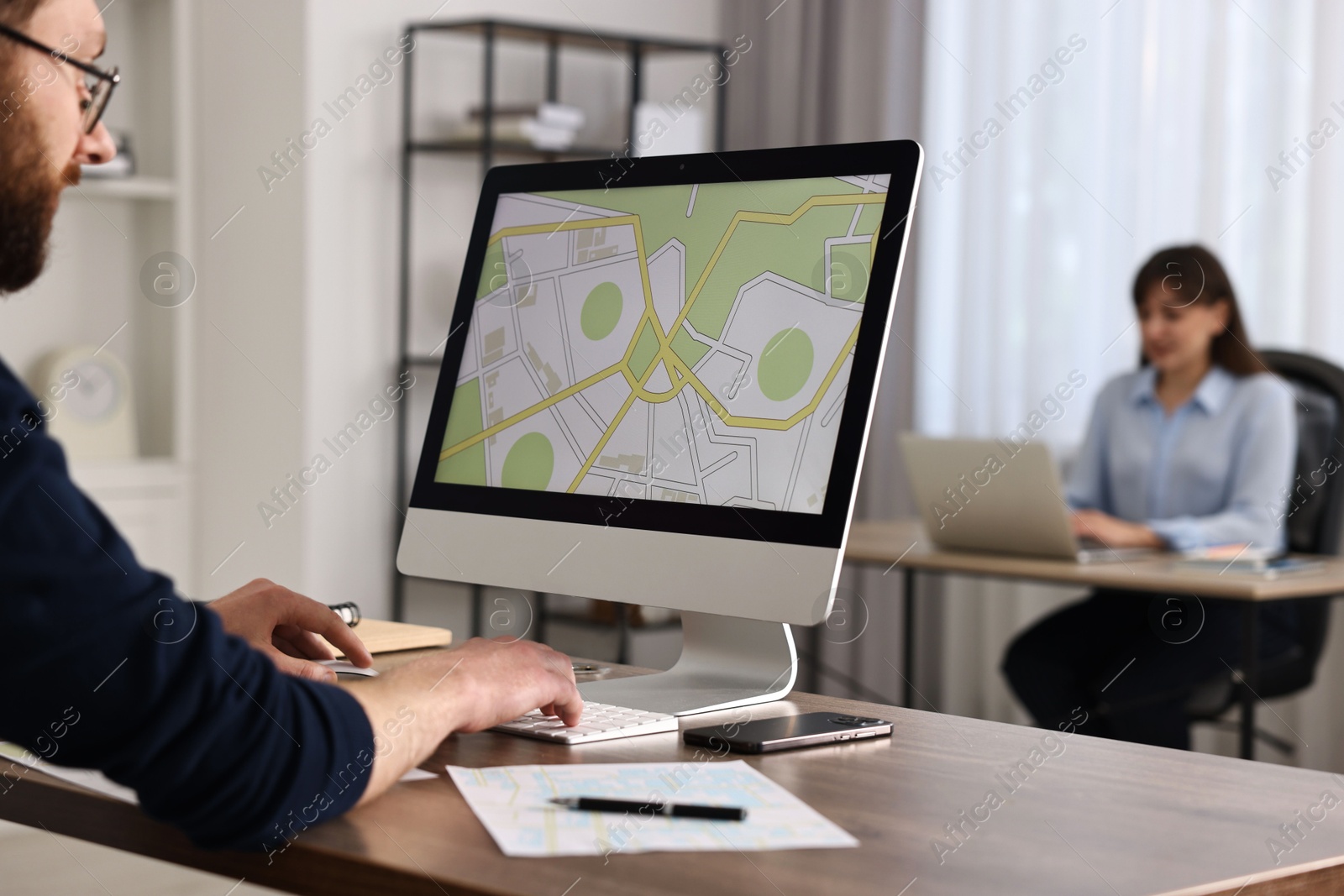 Photo of Cartographer working with cadastral map on computer at wooden table in office, closeup