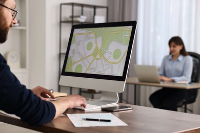 Cartographer working with cadastral map on computer at wooden table in office, closeup