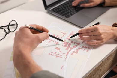 Photo of Cartographers working with cadastral map at white table in office, closeup