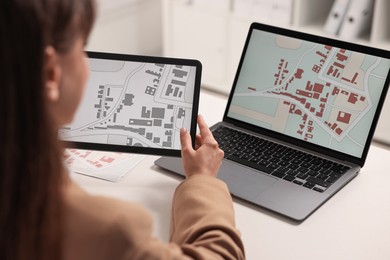 Photo of Cartographer working with cadastral maps on devices at white table in office, closeup