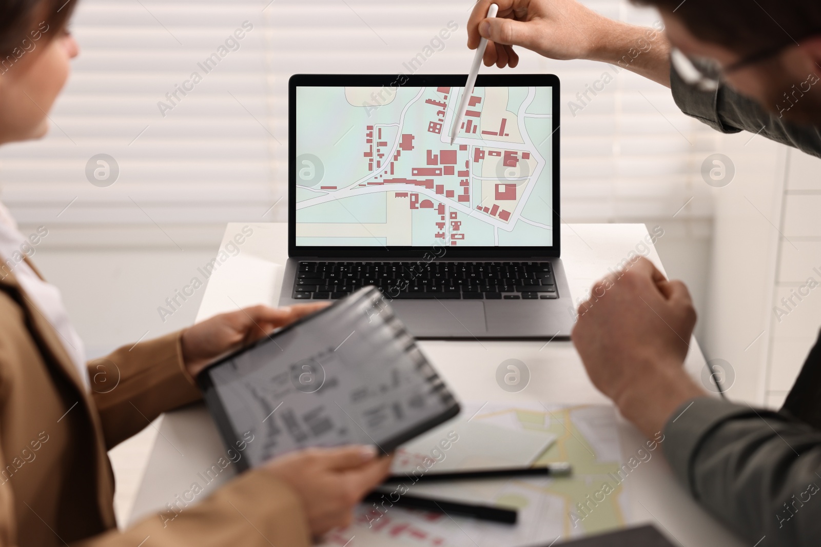 Photo of Cartographers working with cadastral map on laptop at white table in office, closeup