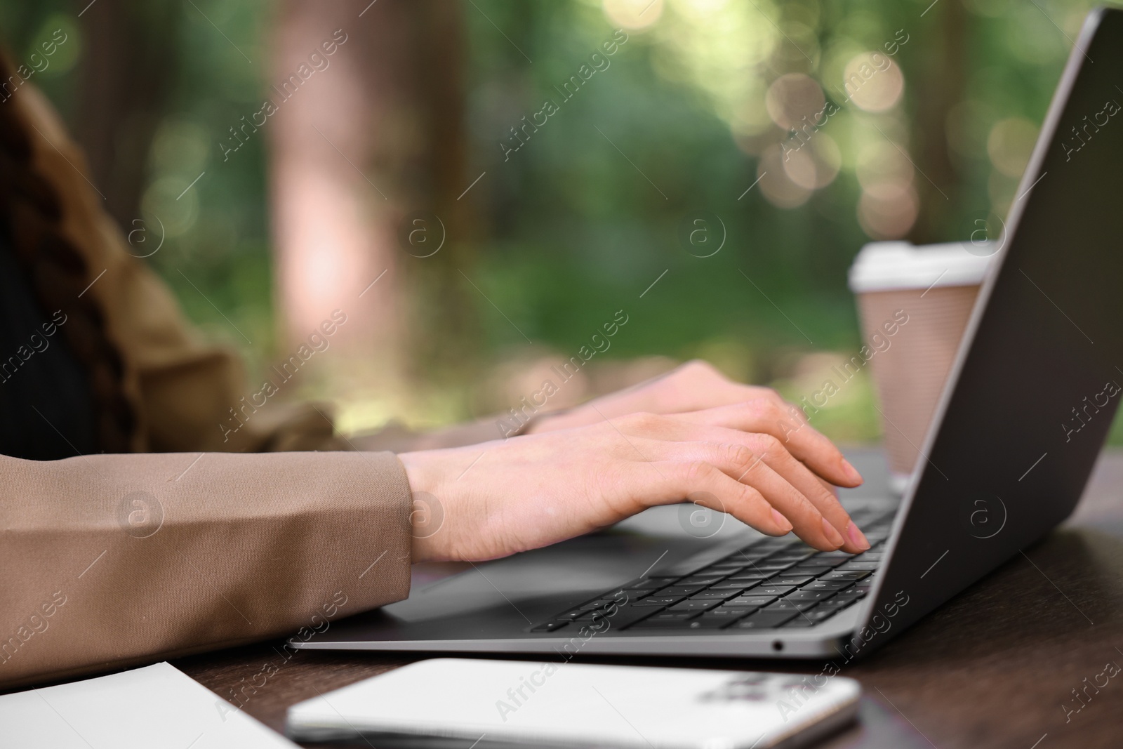 Photo of Businesswoman working with laptop at wooden table outdoors, closeup. Remote job