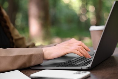 Photo of Businesswoman working with laptop at wooden table outdoors, closeup. Remote job