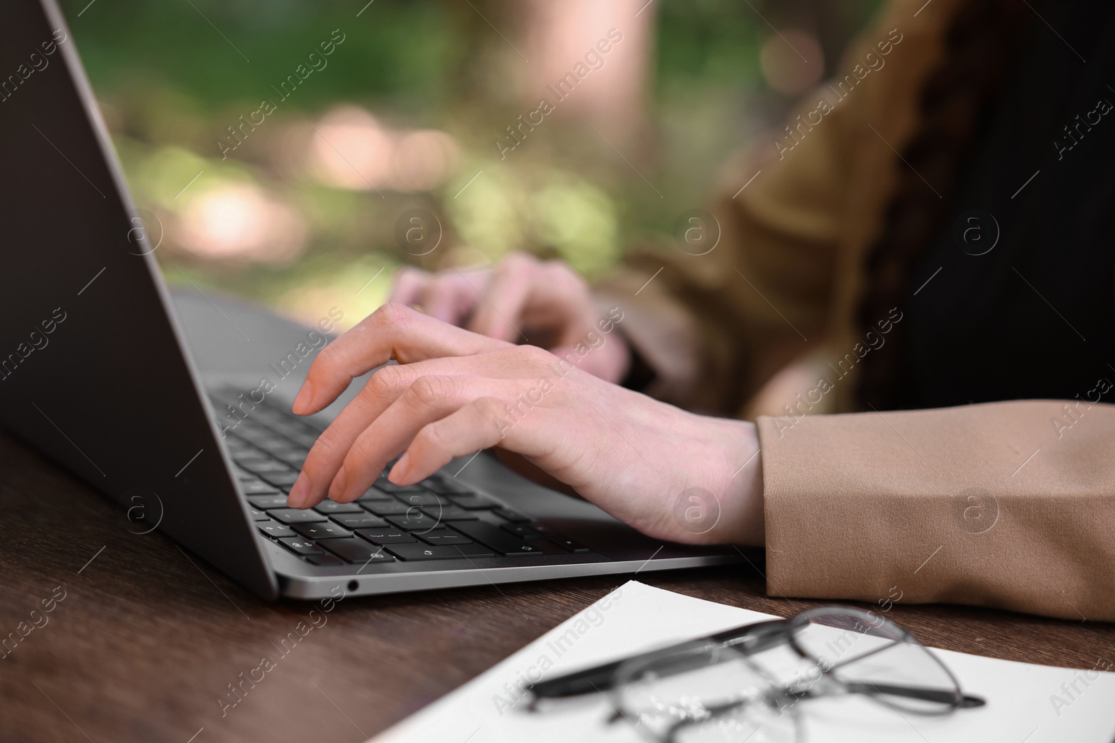 Photo of Businesswoman working with laptop at wooden table outdoors, closeup. Remote job