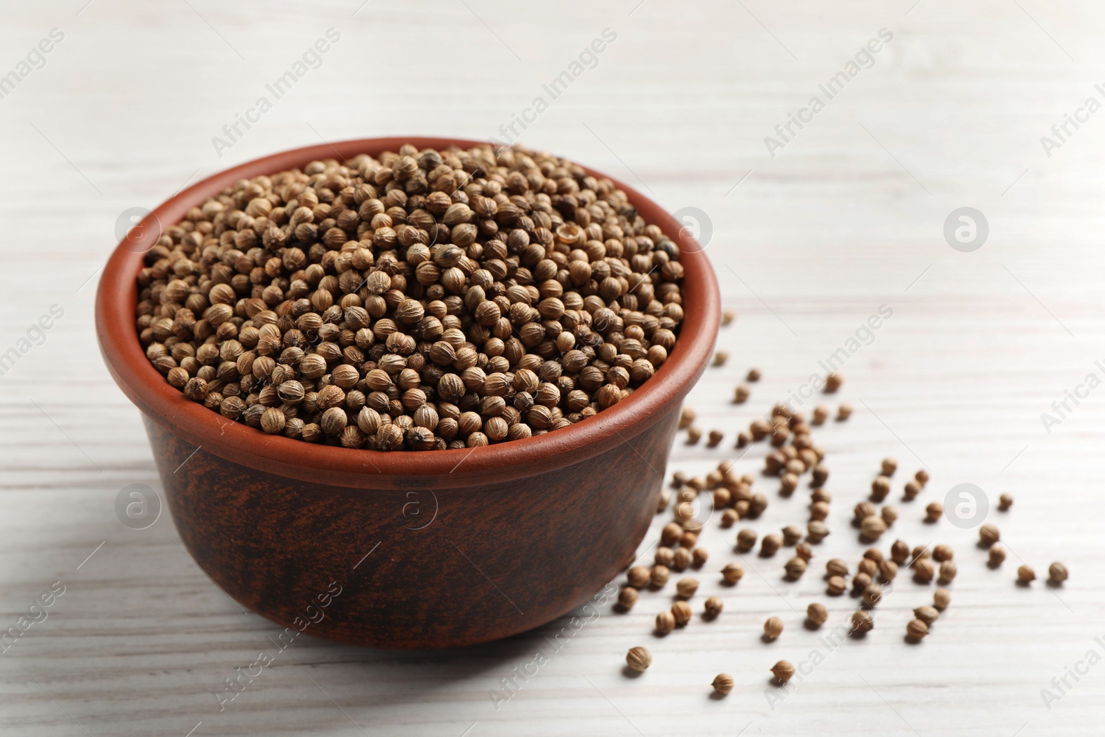 Photo of Dried coriander seeds in bowl on wooden table