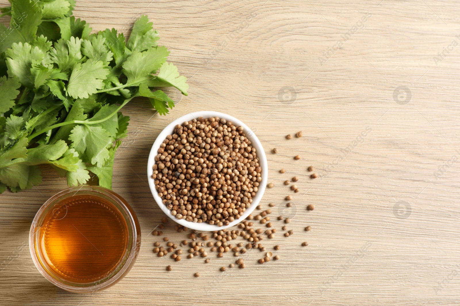 Photo of Dried coriander seeds in bowl, oil and green leaves on wooden table, top view. Space for text