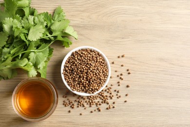 Photo of Dried coriander seeds in bowl, oil and green leaves on wooden table, top view. Space for text