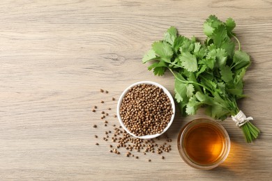 Dried coriander seeds in bowl, oil and green leaves on wooden table, top view. Space for text