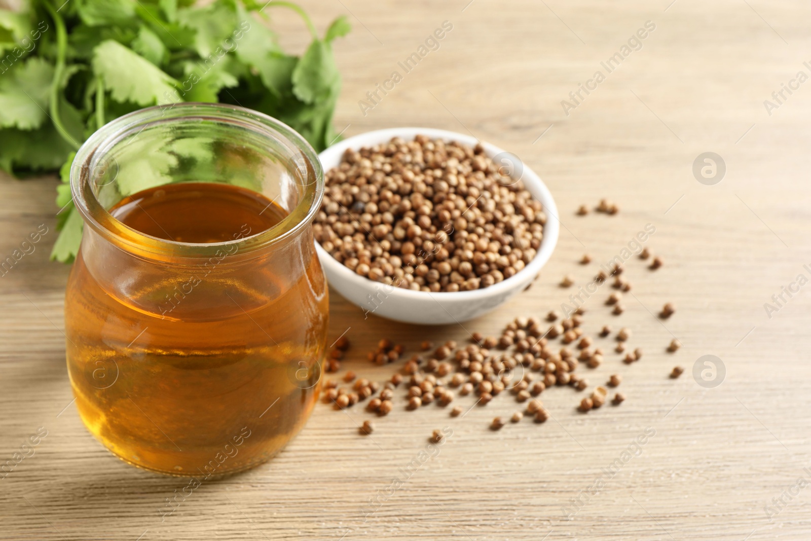 Photo of Dried coriander seeds in bowl, oil and green leaves on wooden table