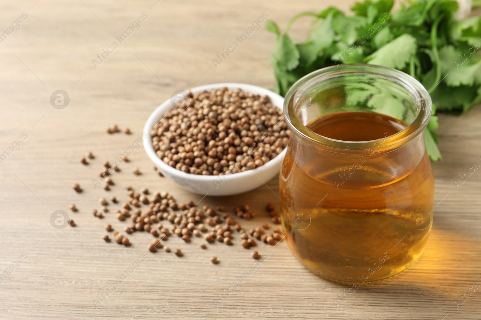 Photo of Dried coriander seeds in bowl, oil and green leaves on wooden table