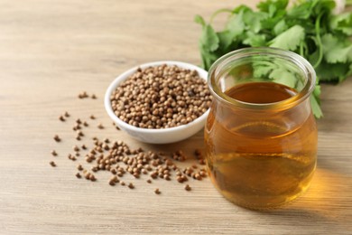 Dried coriander seeds in bowl, oil and green leaves on wooden table