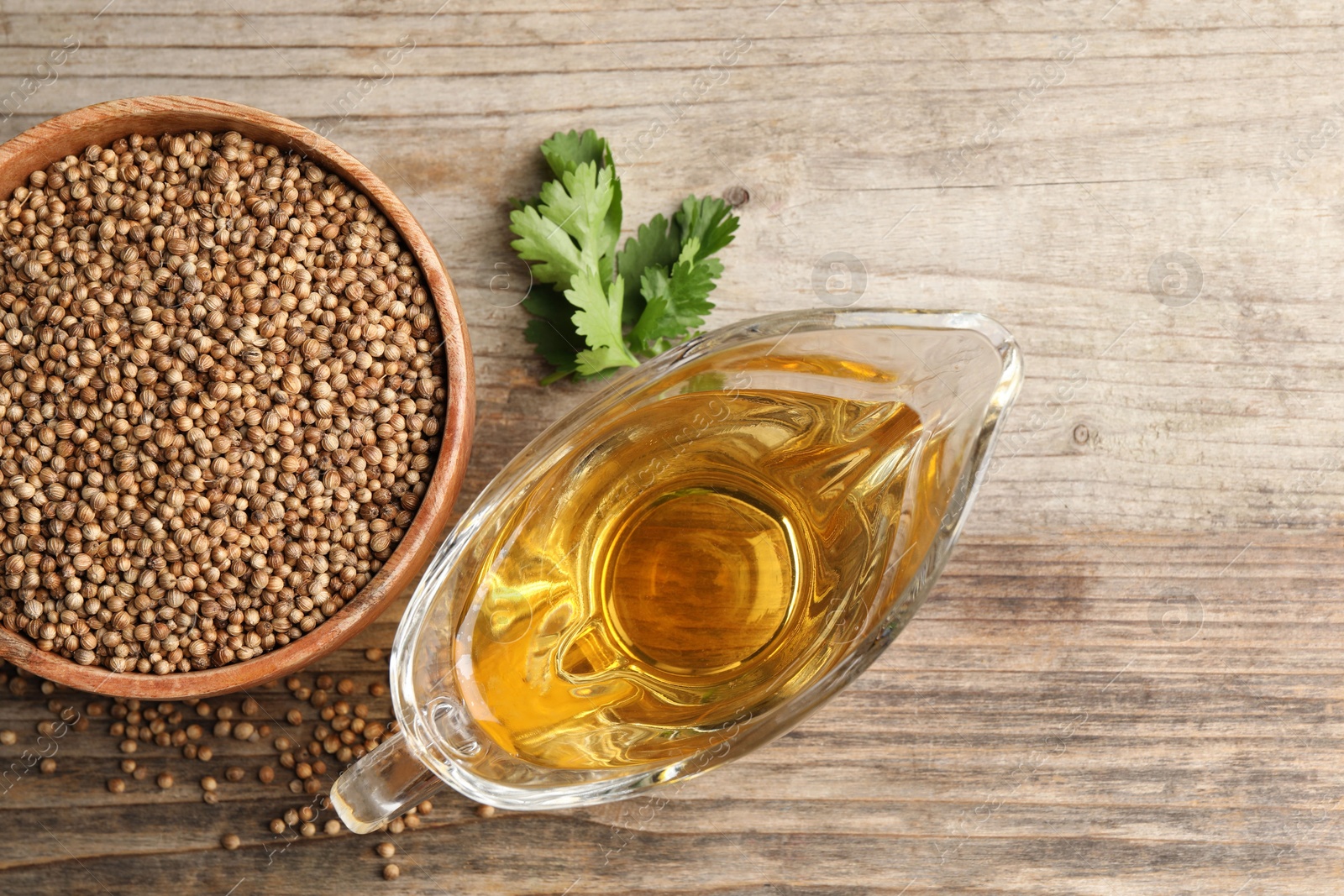 Photo of Dried coriander seeds in bowl, oil and green leaves on wooden table, top view. Space for text