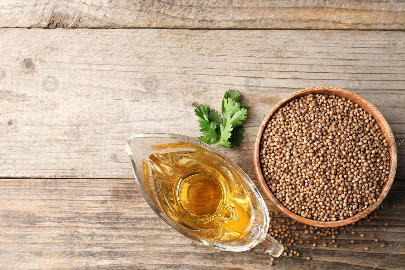 Photo of Dried coriander seeds in bowl, oil and green leaves on wooden table, top view. Space for text