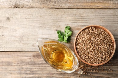 Dried coriander seeds in bowl, oil and green leaves on wooden table, top view. Space for text